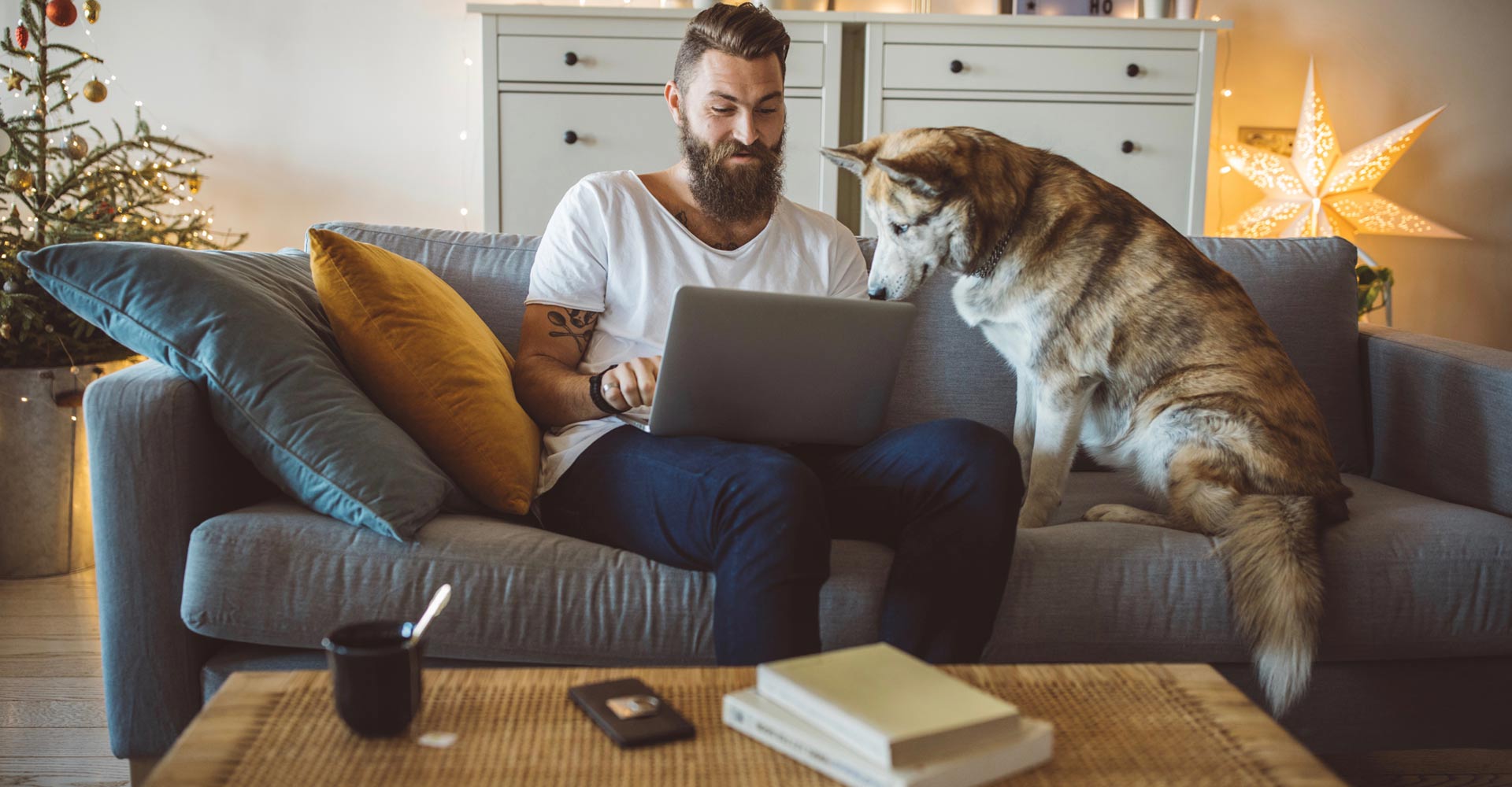 Mann mit Laptop auf Sofa und Hund